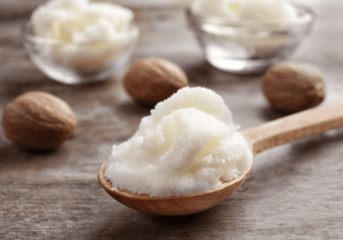 Unrefined shea butter in a wooden spoon with whole shea nuts in the background.