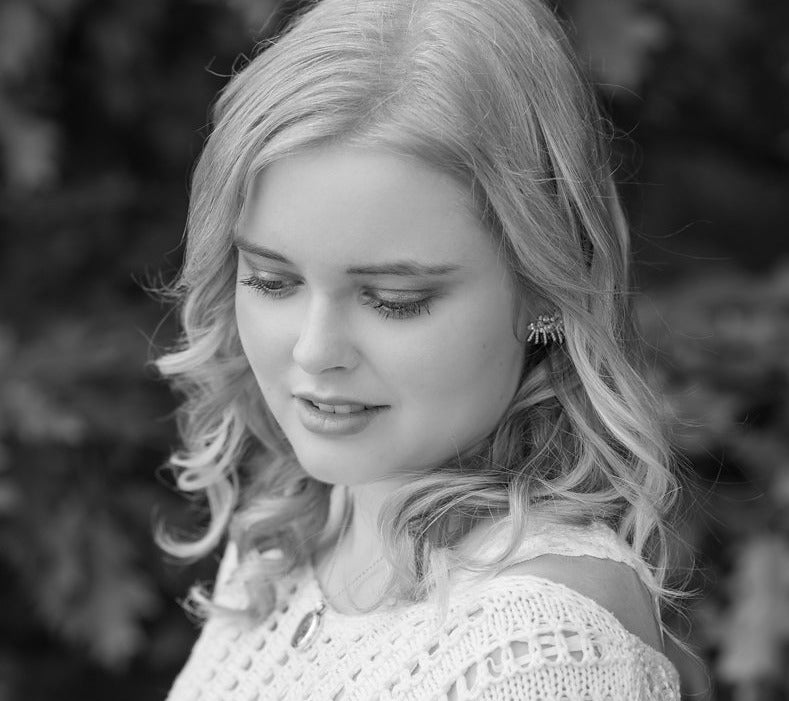 Natural skincare products. A black and white photo of a pretty blond girl with beautiful skin wearing a cream knit sweater looking down, with georgian bay windswept pines in the background. 