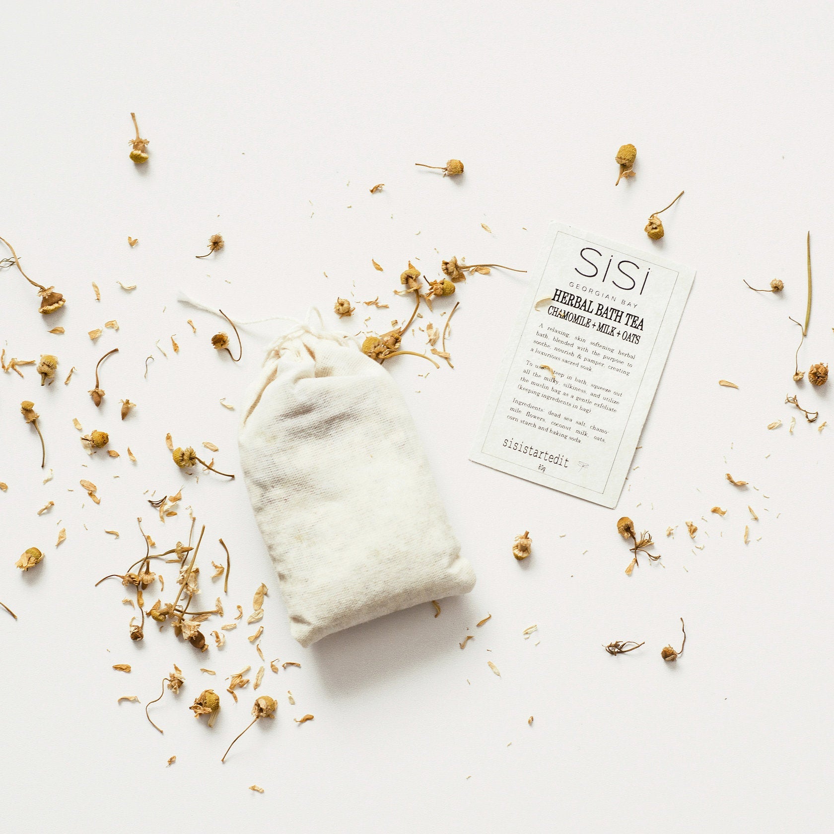 a pretty styled photo of a sisi georgian bay herbal bath tea in a muslin bag on a creamy background with chamomile flowers sprinkled around