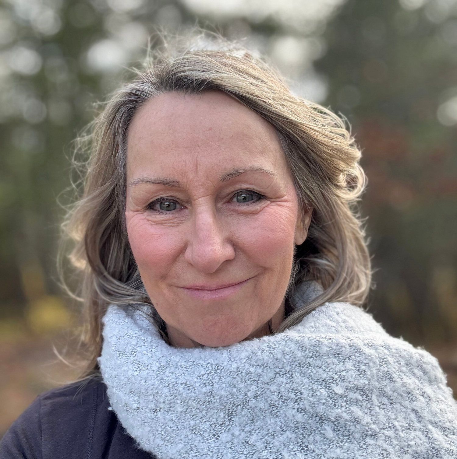 Andrea Tranter - Founder of SiSi Georgian Bay in outdoor setting with blurred forest background wearing fluffy light grey scarf.