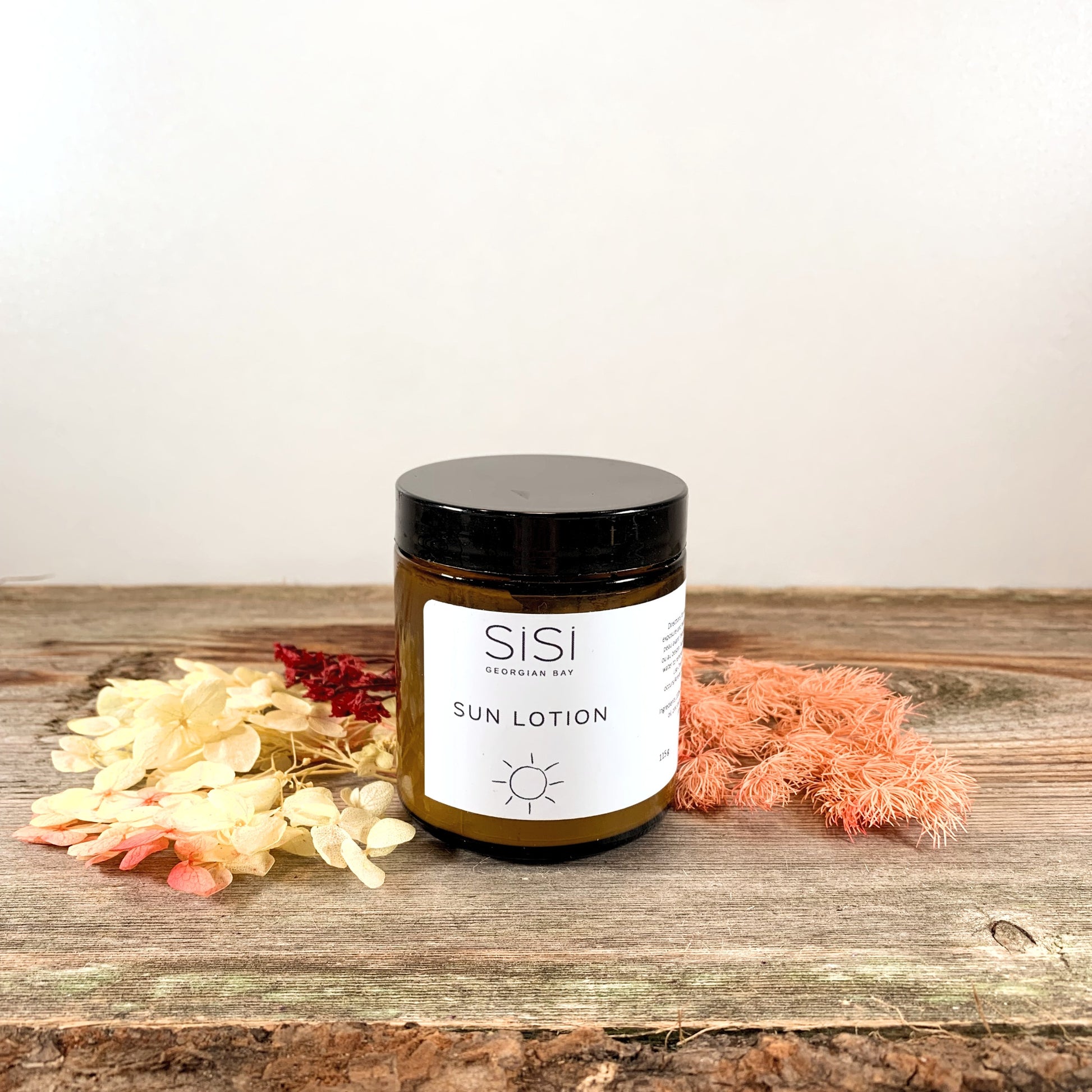 Natural skincare products - Natural Sun Protection - SiSi Georgian Bay Sun Lotion in an amber glass jar on a rustic wooden surface with pretty colourful flowers spread out around it