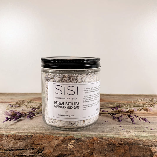 A jar of SiSi Georgian Bay herbal bath tea in a jar on a live edge slab of wood with flowers and greenery around it