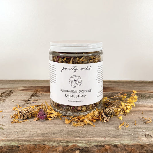 Home Spa Products - SiSi Georgian Bay "pretty wild" facial steams in a clear glass jar on a rustic wooden surface with flowers and herbs sprinkled around it