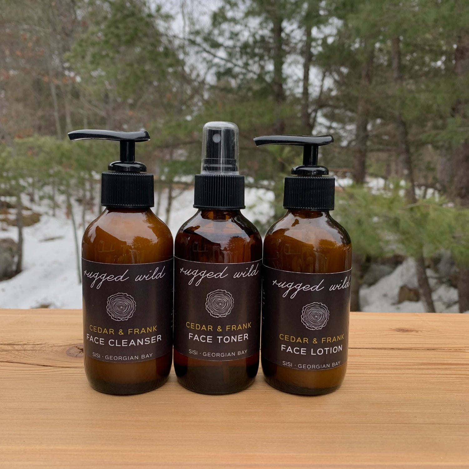 Natural face care for him - natural skincare products - SiSi Georgian Bay  northern ontario "rugged wild" face care trio set on a wooden table outside in nature with evergreen trees and snow covered ground in the background